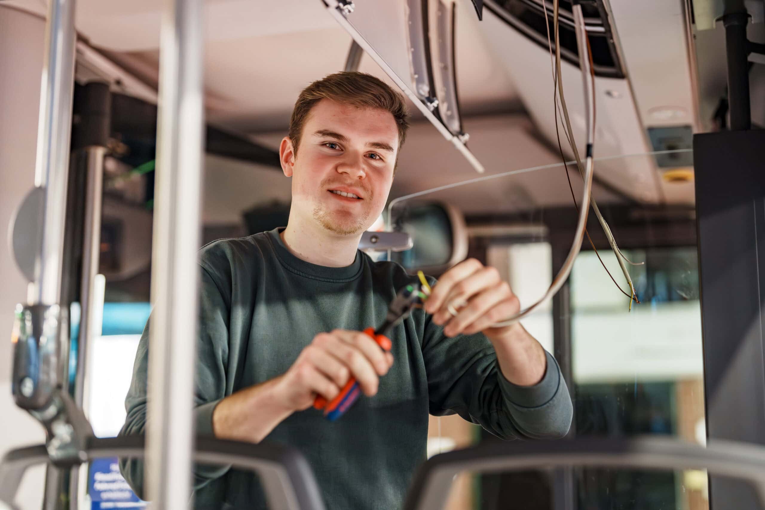 Unser Kollege Alexander steht in einem Bus und hält eine kleine Zange und ein Kabel in der Hand.
