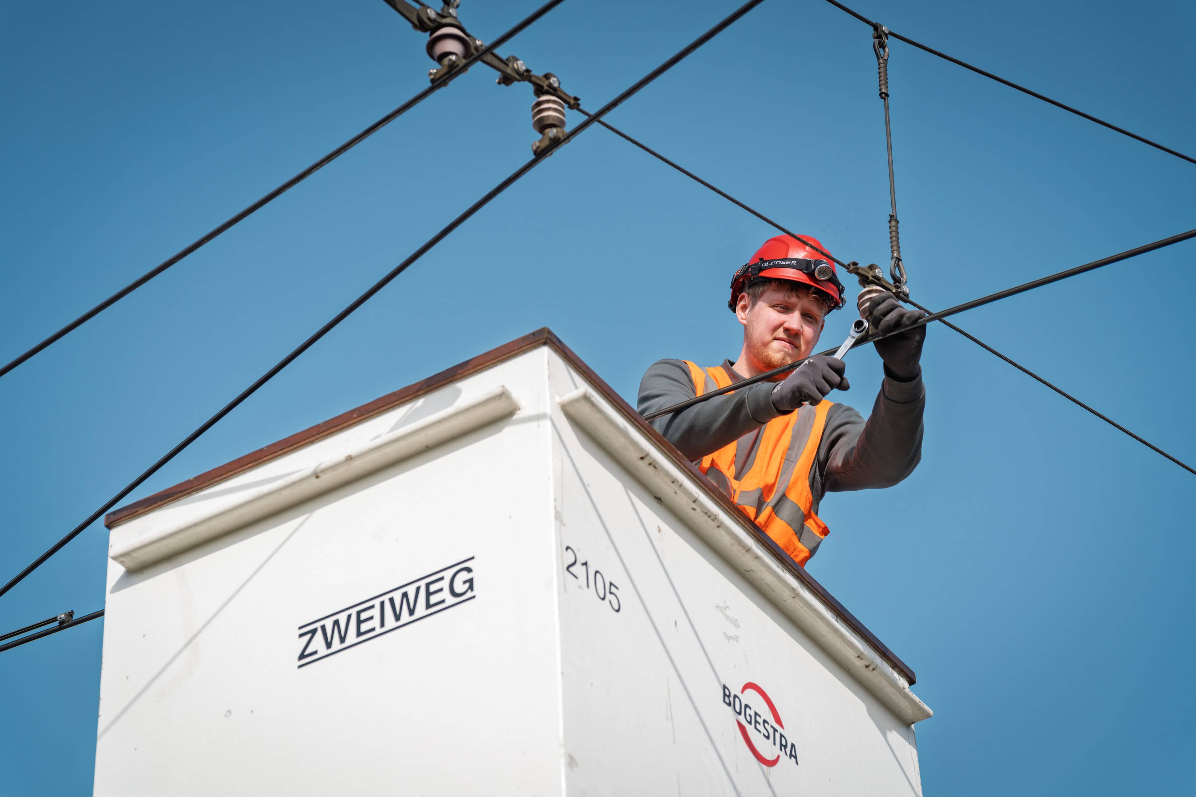 Eine Person in Warnkleidung arbeitet im Korb eines Hubarbeitswagens an einer Fahrleitung.
