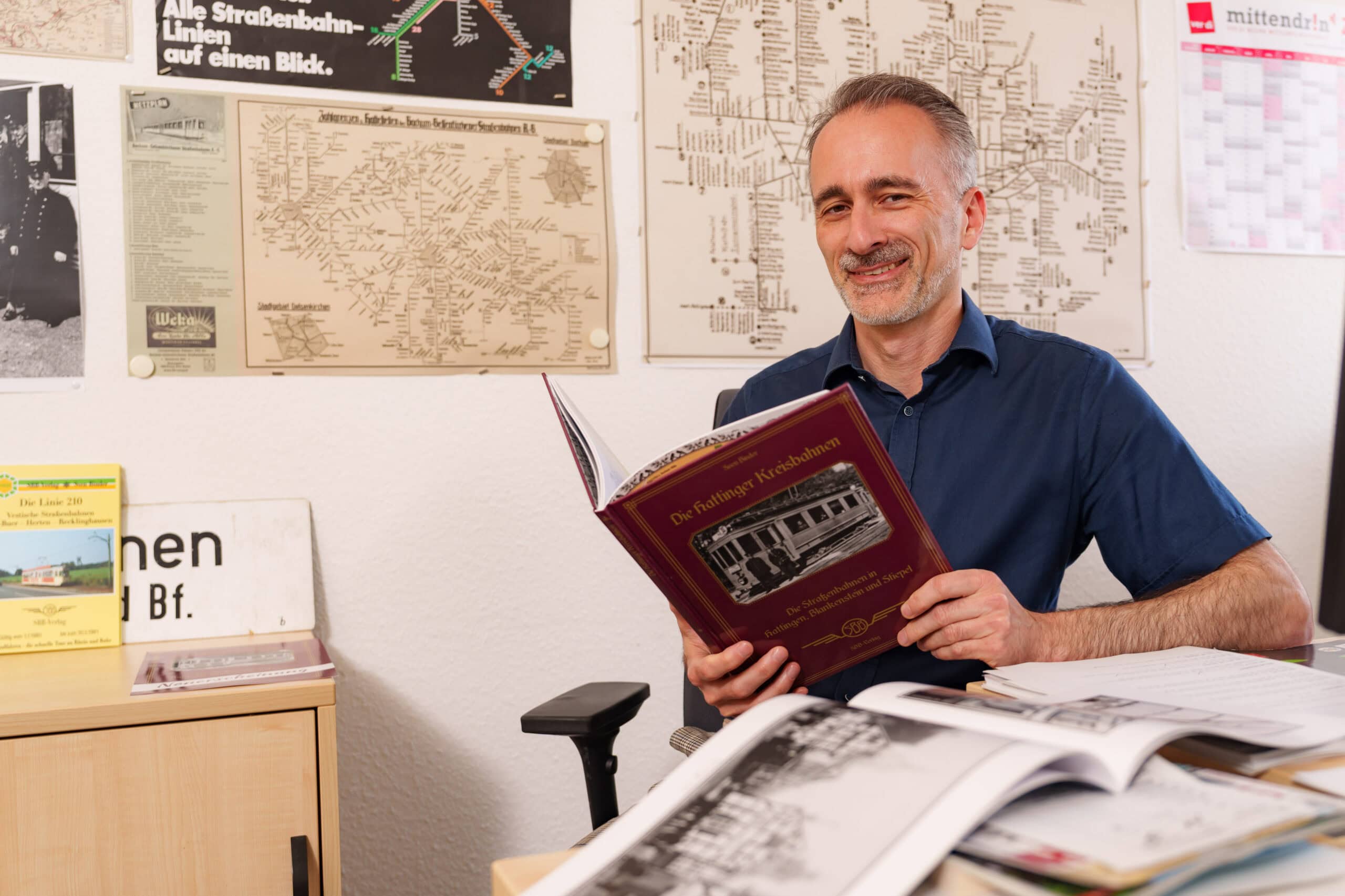 Unser Kollege Sven sitzt an seinem Schreibtisch. In der Hand hält er sein Buch "Die Hattinger Kreisbahnen".