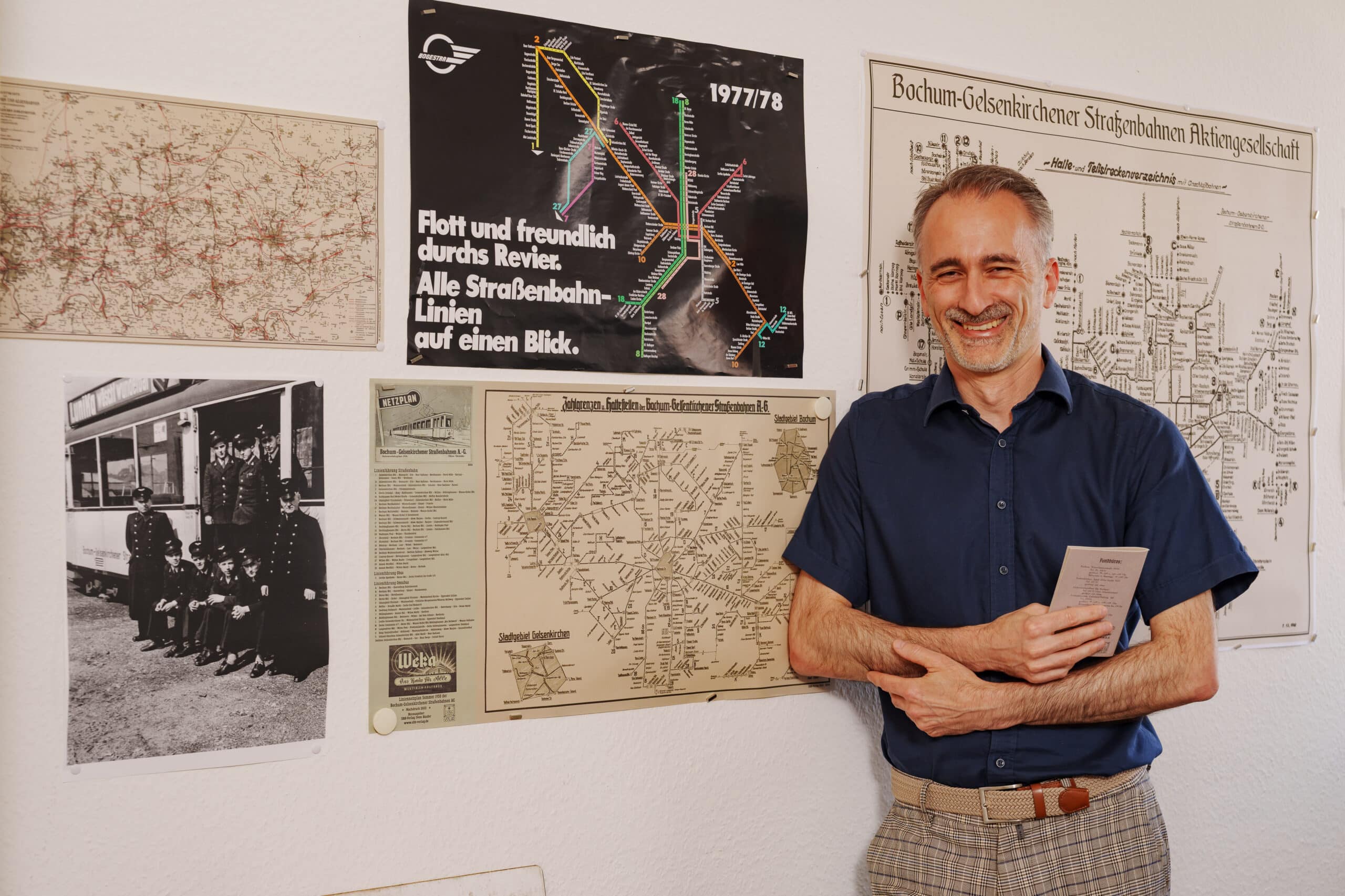 Unser Kollege Sven lehnt an der Wand seines Büros. Hinter ihm sind viele alte Liniennetzpläne.